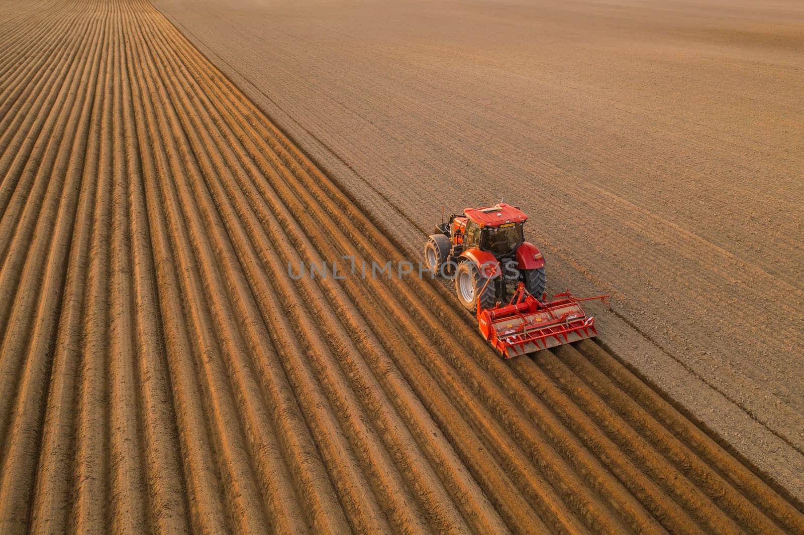 PRAGUE , CZECH REPUBLIC - MARCH 18 2022: Tractor drives preparing beds for planting seedlings in cultivated soil. Heavy machine tills on field helping with agriculture aerial view