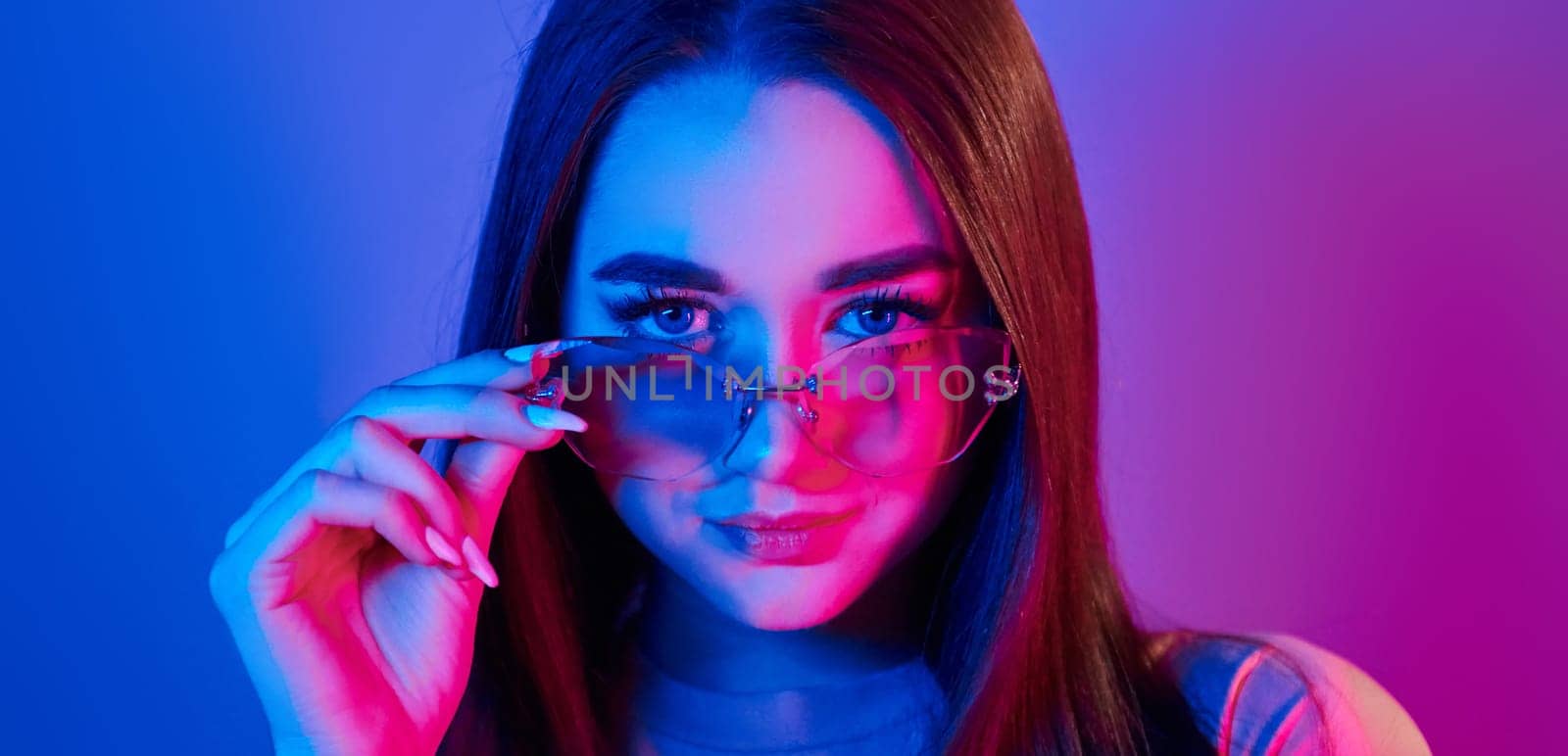 Neutral facial expression. Fashionable young woman standing in the studio with neon light.