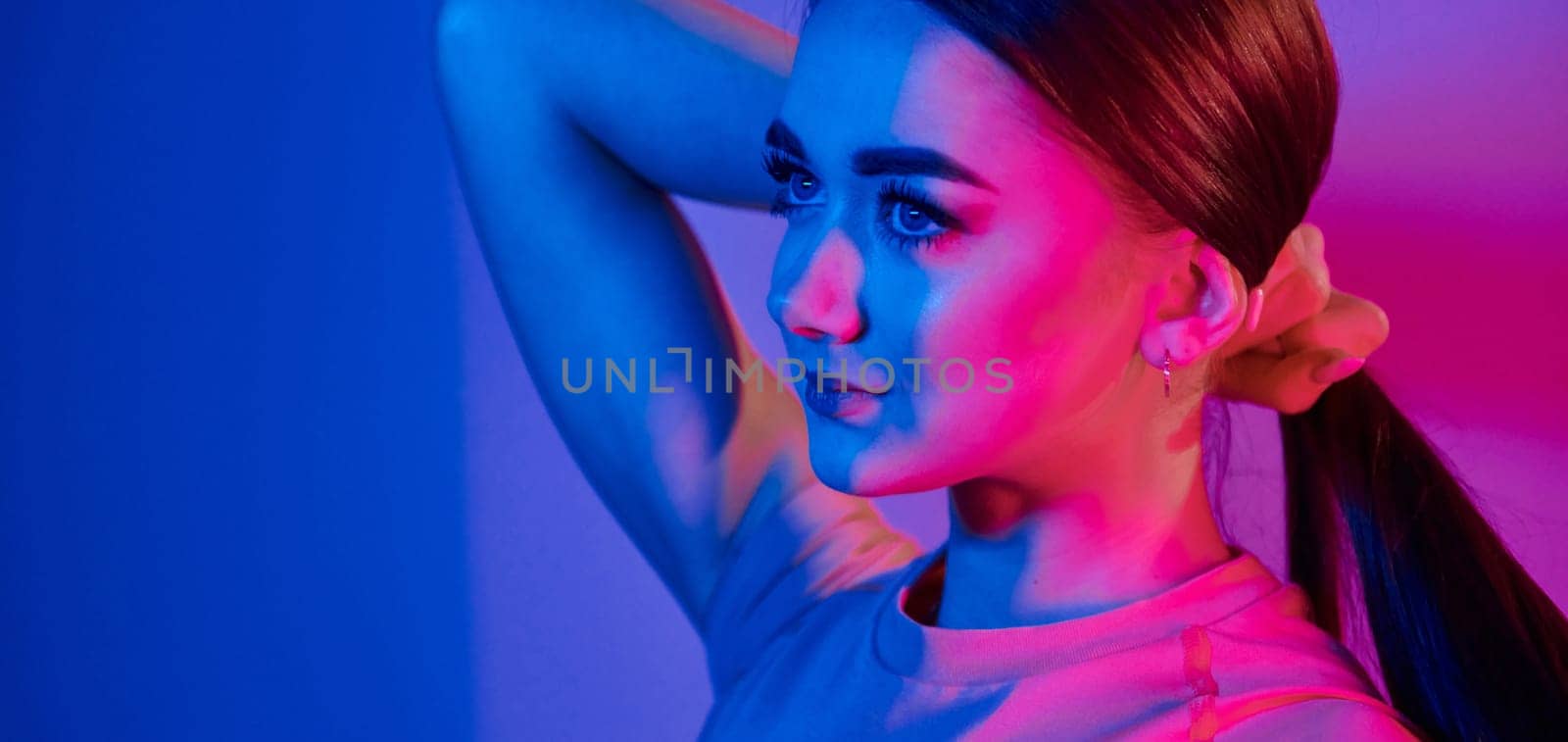 Side view. Fashionable young woman standing in the studio with neon light.