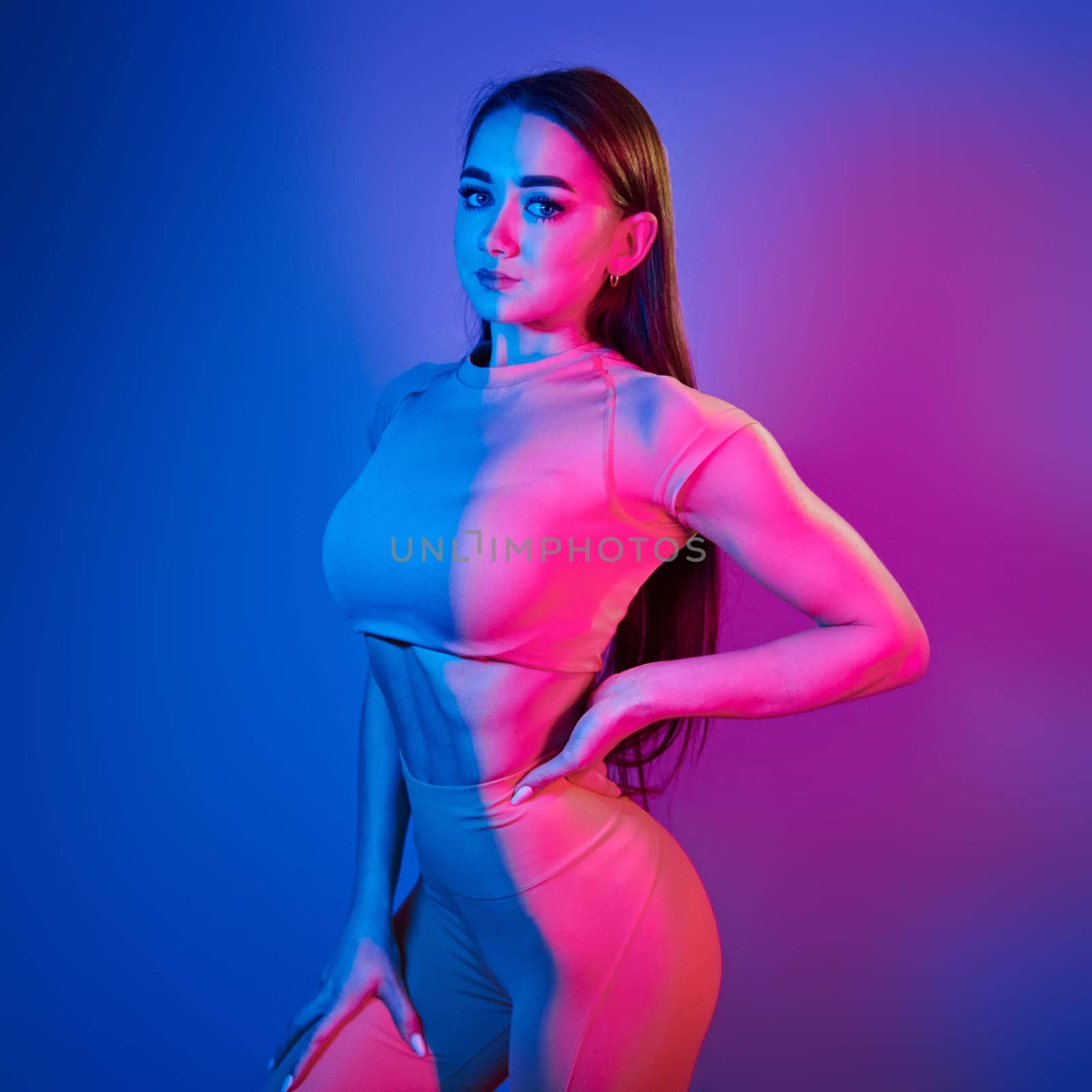 Slim body. Fashionable young woman standing in the studio with neon light by Standret