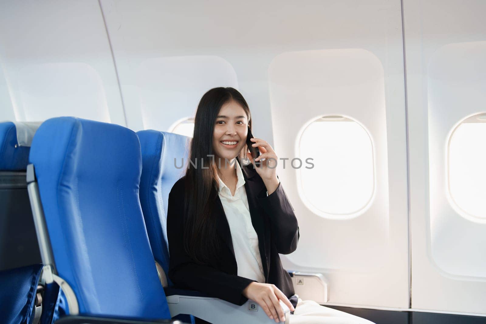 Asian business woman passenger sitting on business class luxury plane while working using smart phone mobile talking or video conference and travel concept.