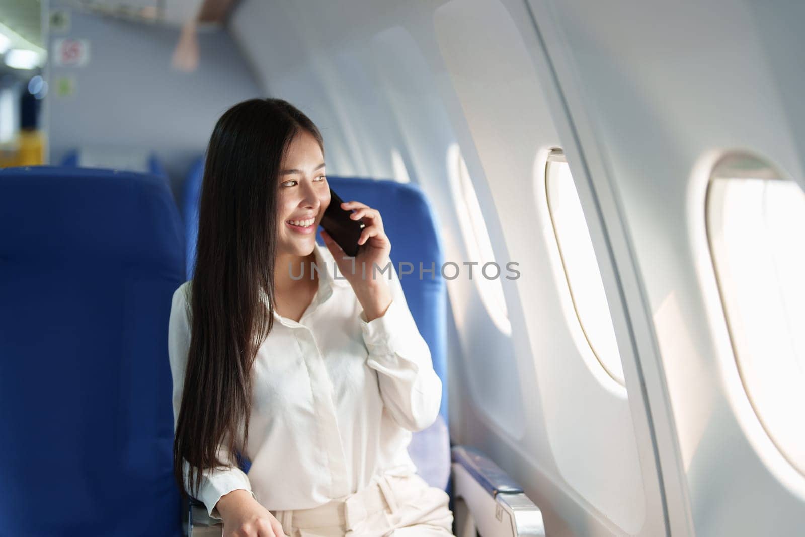 Asian business woman passenger sitting on business class luxury plane while working using smart phone mobile talking or video conference and travel concept.