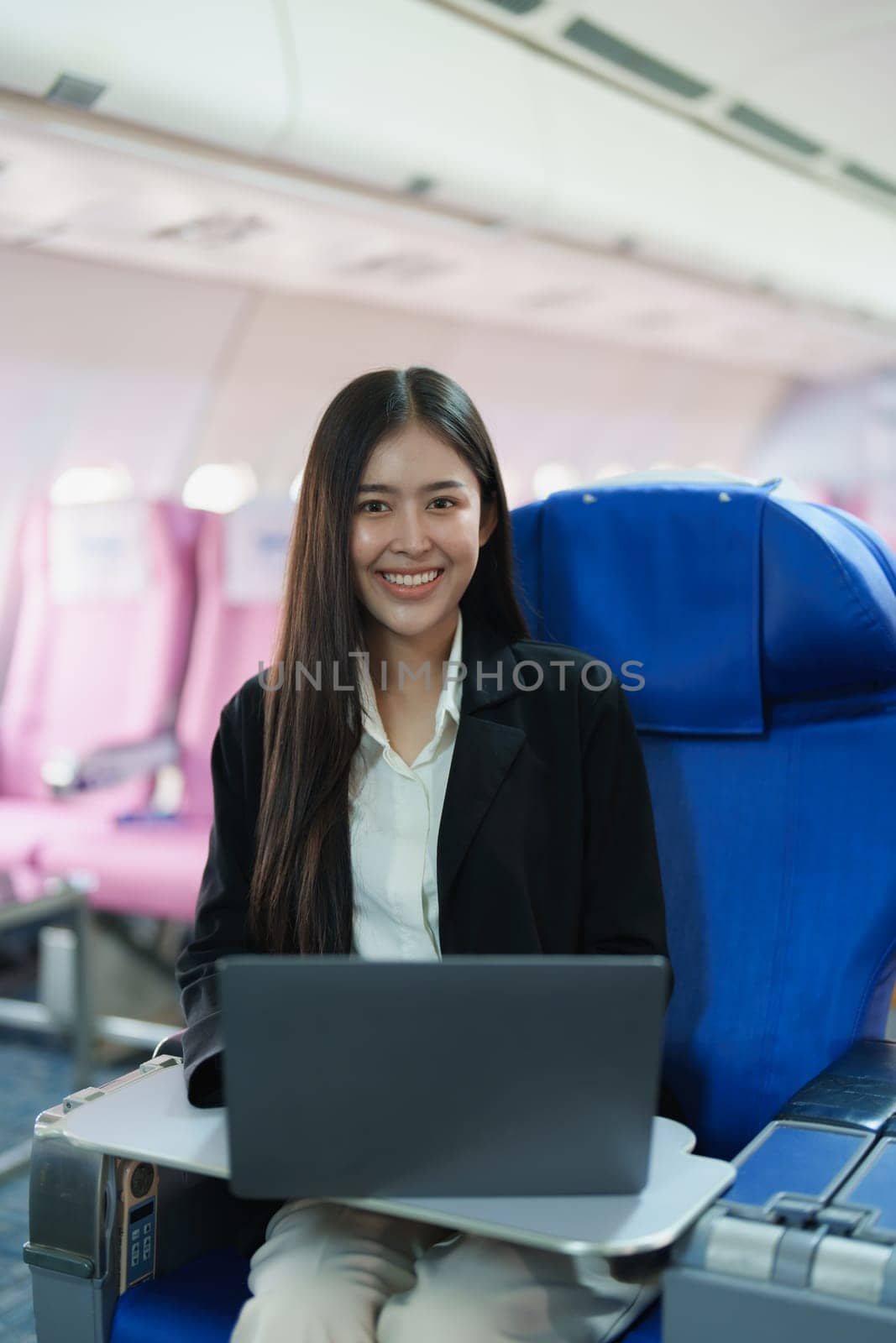 Asian business woman passenger sitting on business class plane while working on laptop computer with simulated space using on board wireless connection by Manastrong