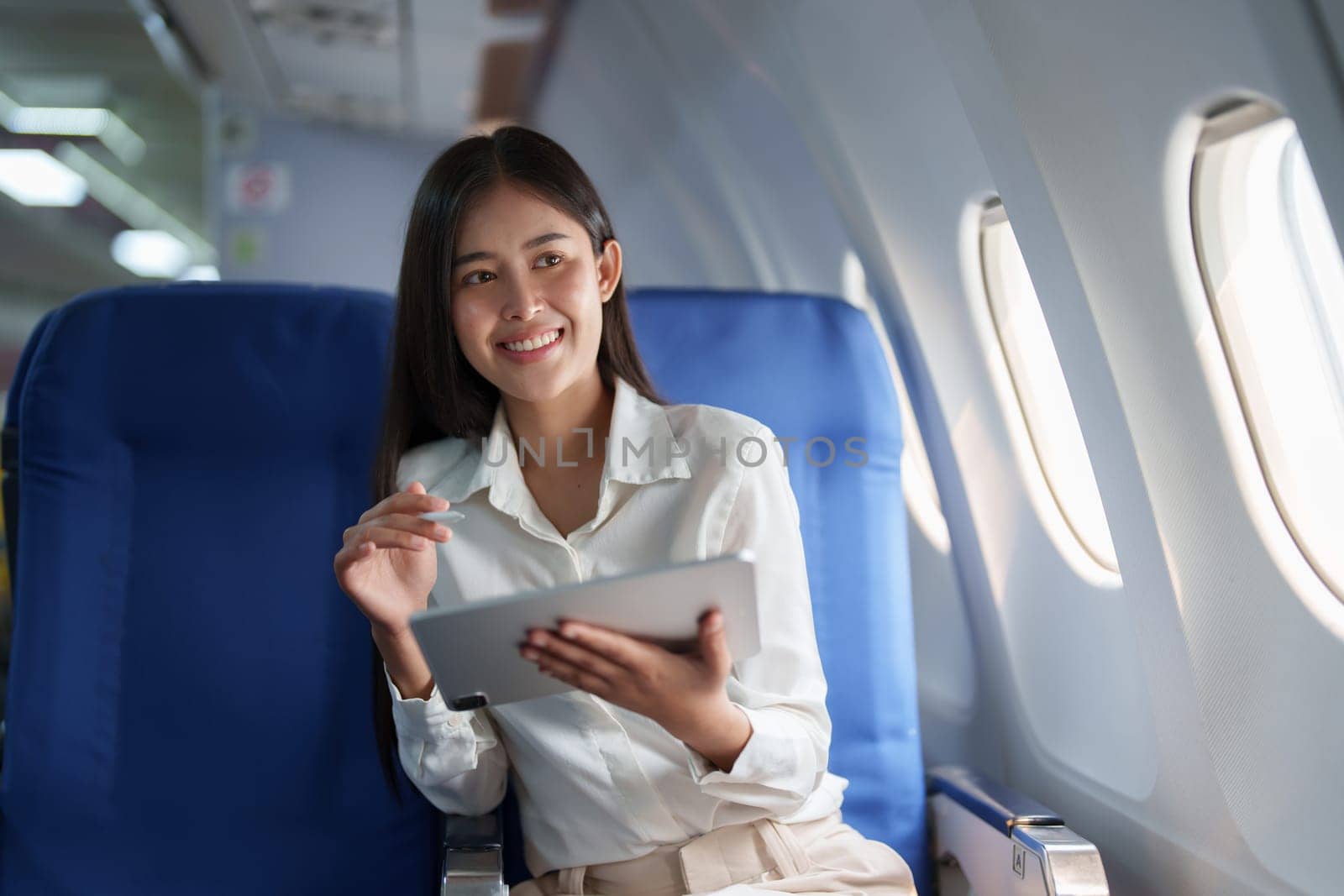 Asian attractive business woman passenger sitting on business class luxury plane while tablet computer while travel concept by Manastrong