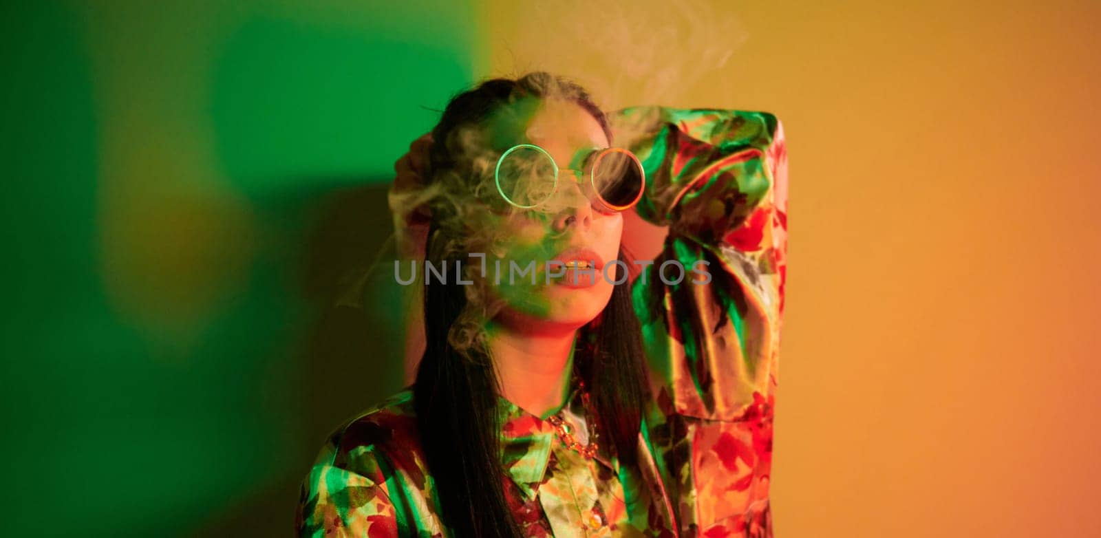 Smoking, activity. Fashionable young woman standing in the studio with neon light.