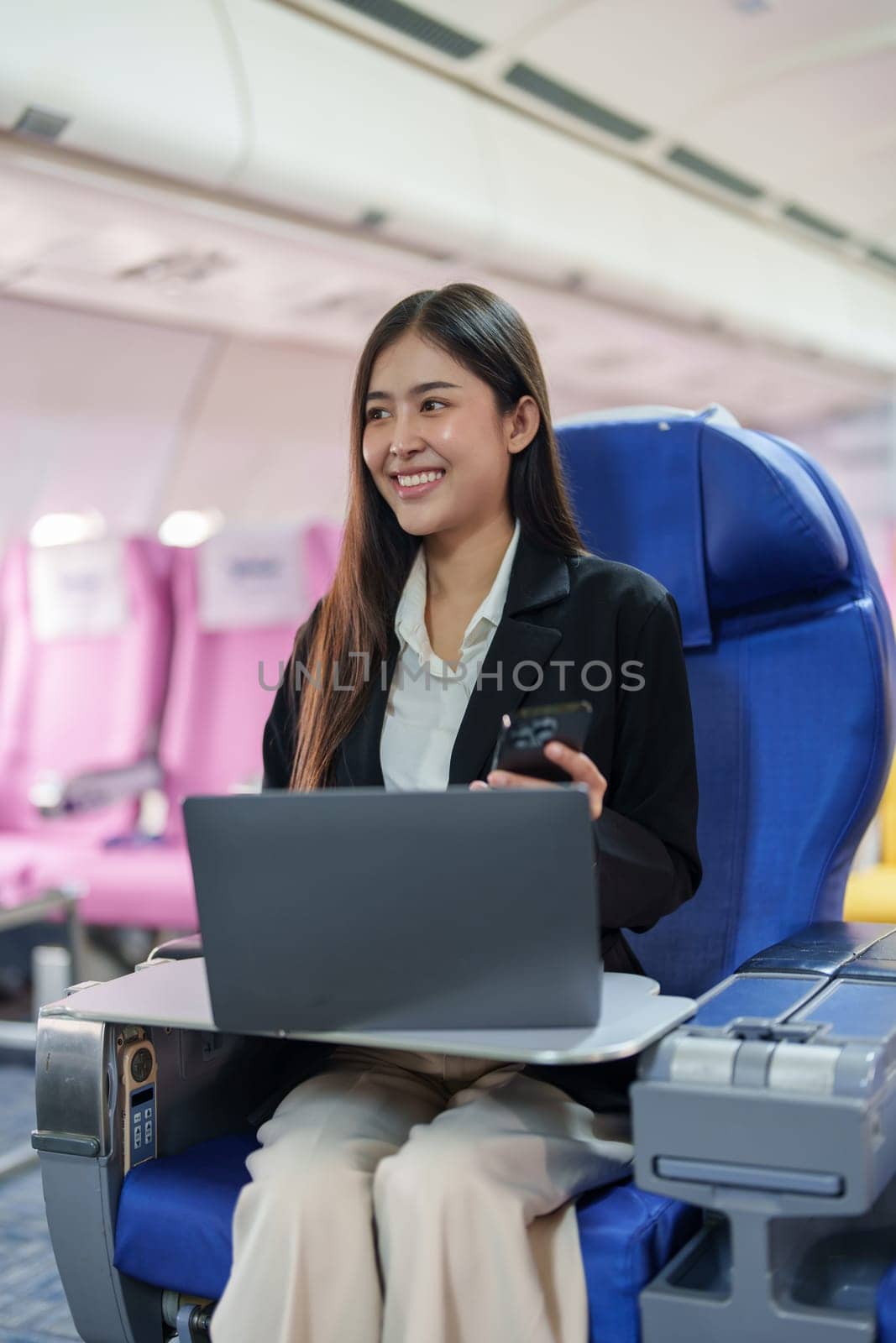 Asian business woman passenger sitting on business class luxury plane while working using smartphone mobile talking and use laptop computer with simulated space using on board wireless connection by Manastrong