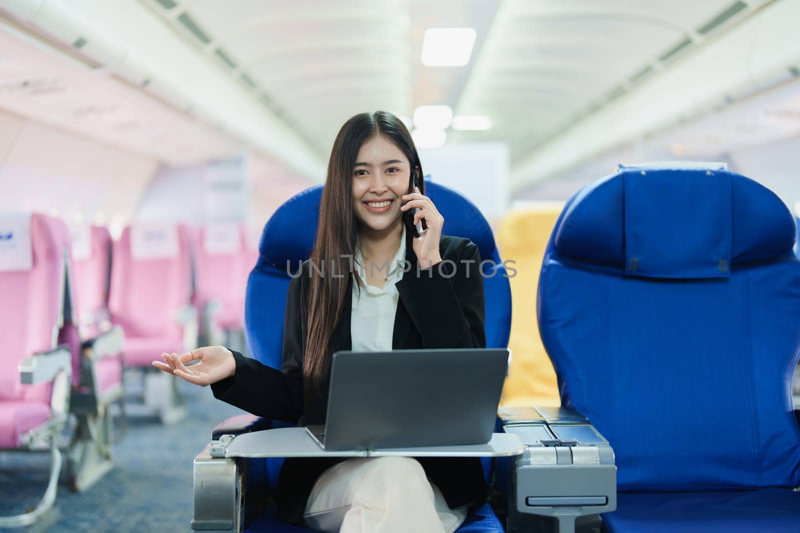 Asian business woman passenger sitting on business class luxury plane while working using smartphone mobile talking and use laptop computer with simulated space using on board wireless connection by Manastrong
