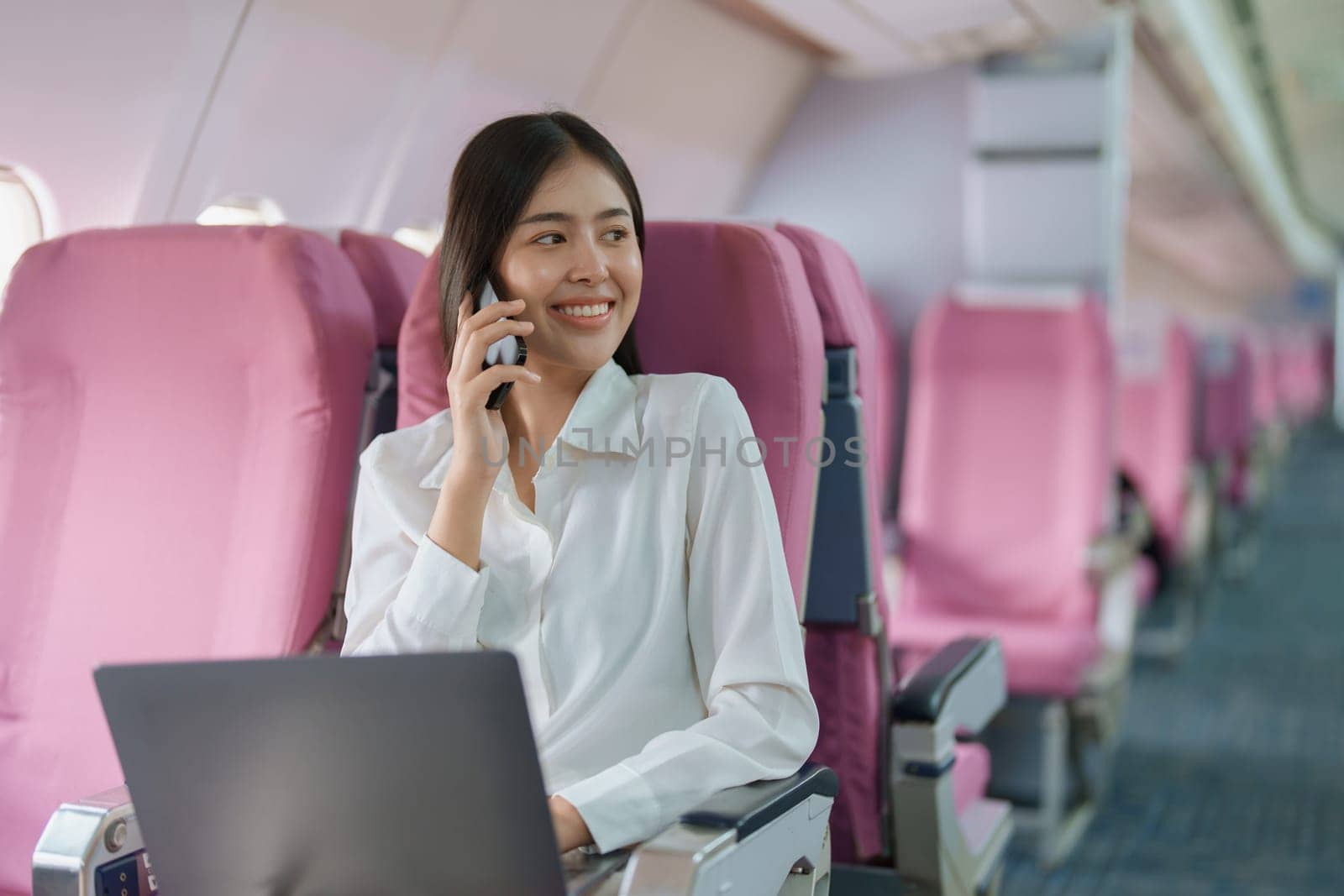 Asian business woman passenger sitting on business class luxury plane while working using smart phone mobile talking or video conference and travel concept by Manastrong