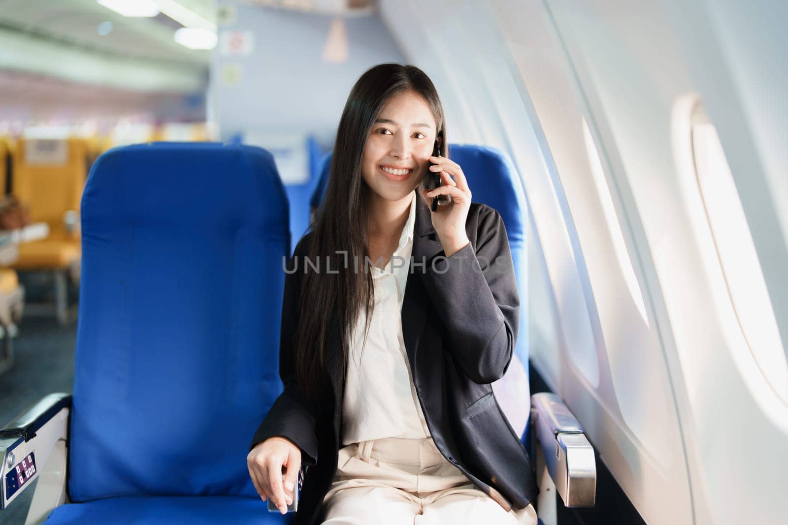 Asian business woman passenger sitting on business class luxury plane while working using smart phone mobile talking or video conference and travel concept by Manastrong