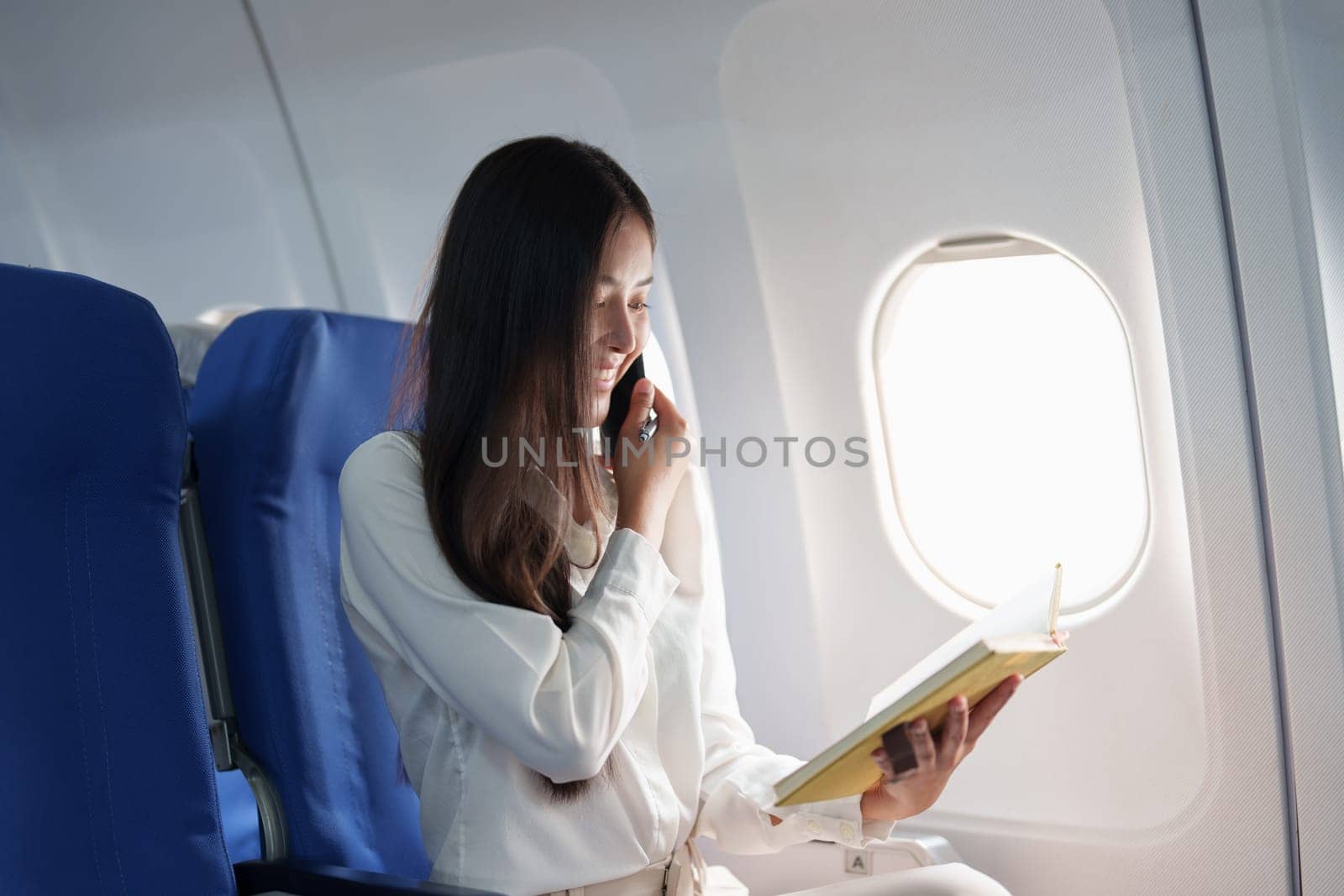 Asian business woman passenger sitting on business class luxury plane while working using smart phone mobile talking and use notebook while travel concept by Manastrong