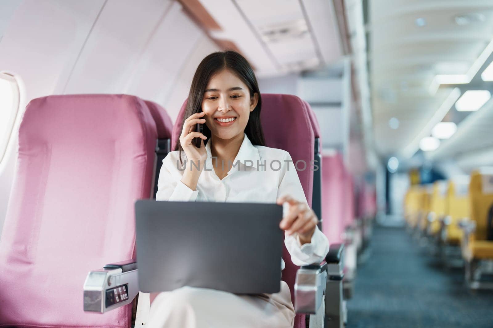 Asian business woman passenger sitting on business class luxury plane while working using smart phone mobile talking or video conference and travel concept.