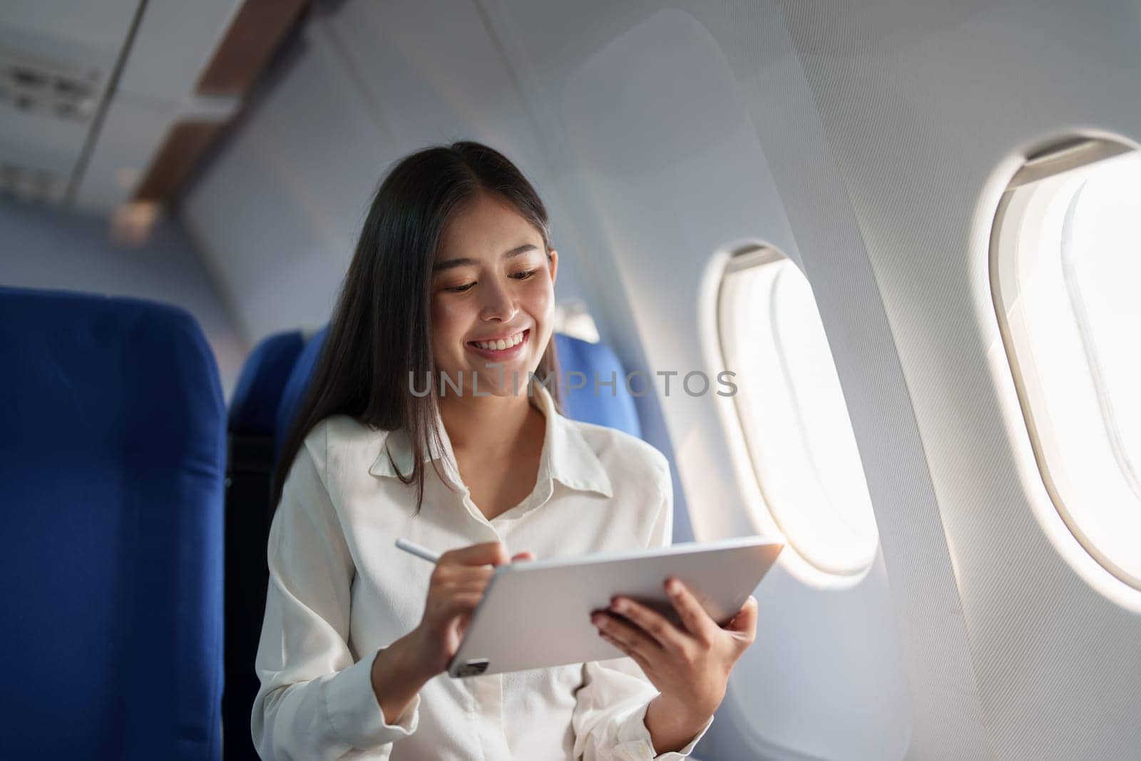 Asian attractive business woman passenger sitting on business class luxury plane while tablet computer while travel concept by Manastrong