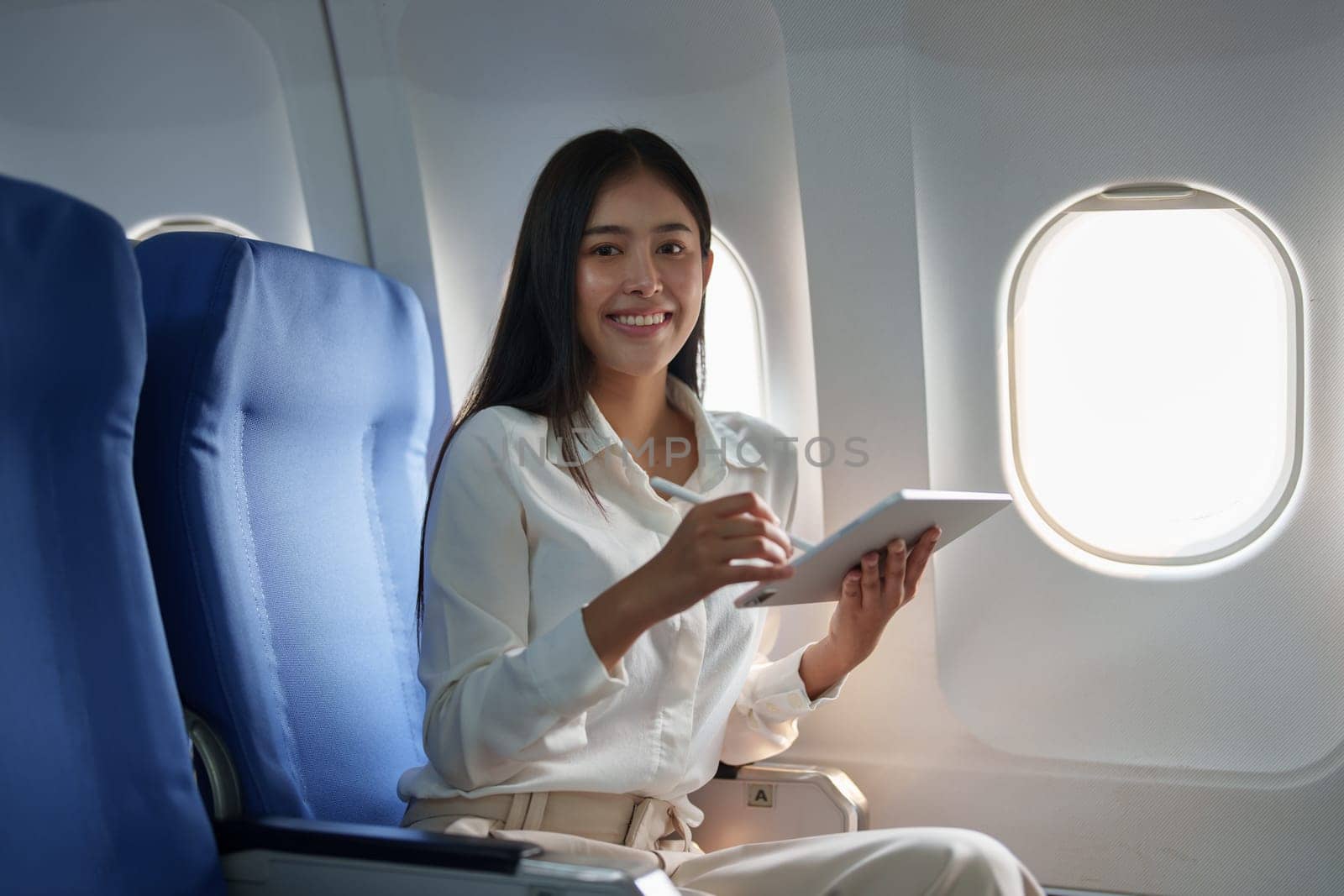 Asian attractive business woman passenger sitting on business class luxury plane while tablet computer while travel concept.