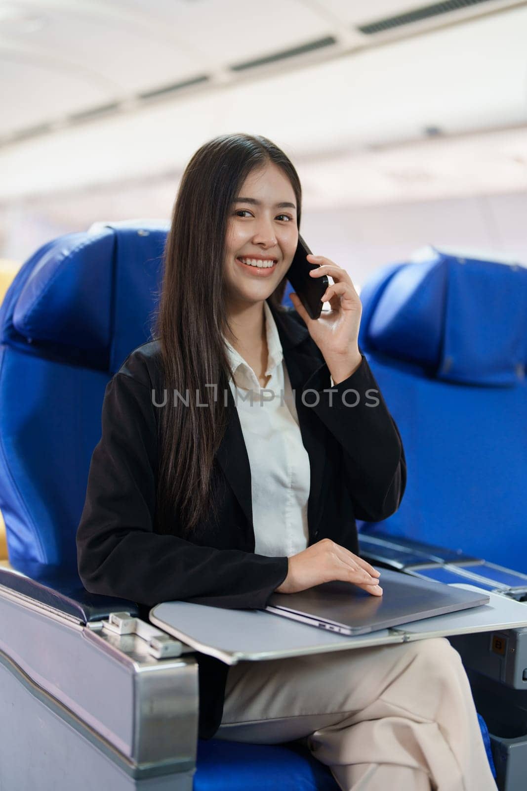 Asian business woman passenger sitting on business class luxury plane while working using smart phone mobile talking and use laptop computer with simulated space using on board wireless connection