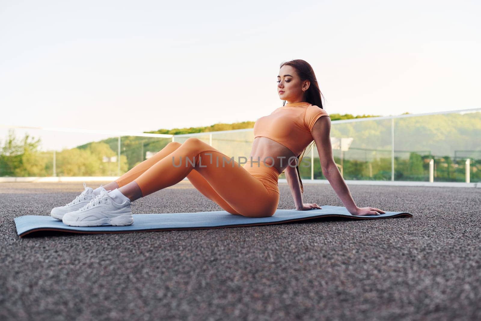 Sky and trees at background. Young woman in sportswear have fitness session outdoors by Standret