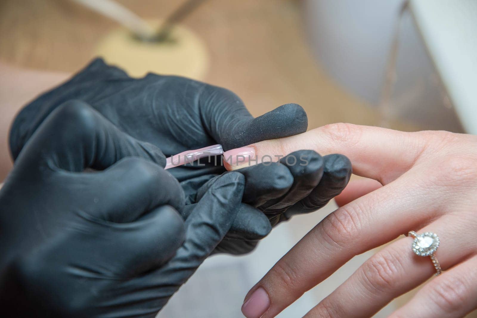 a master does a manicure to a client in a beauty salon and covers her nails with pink varnish. High quality photo