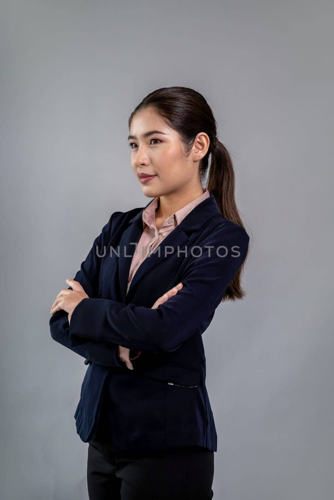 Confident young businesswoman stands on isolated background, posing in formal black suit. Office lady or manager with smart and professional appearance. Enthusiastic