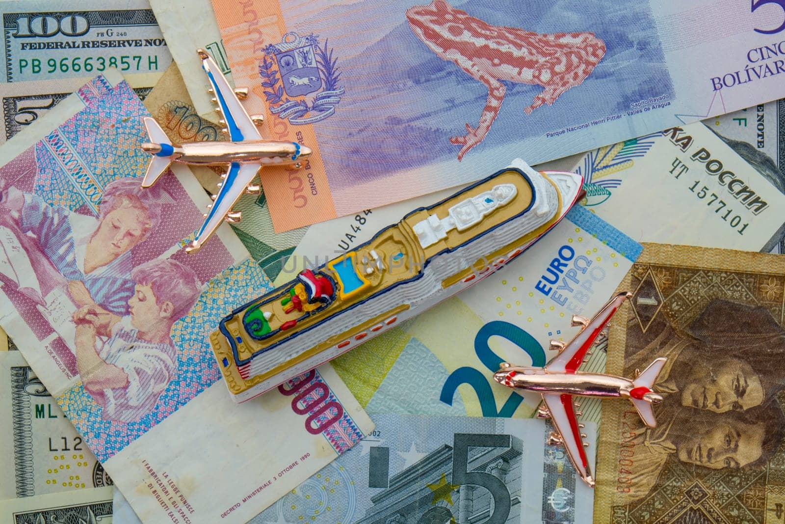 Miniature cruise ship, airplanes sitting on arrangement of international currencies including euro, ruble USD. Concept of high cost of travel. High quality photo