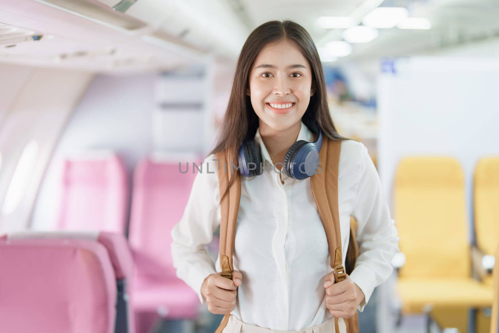 Young asian attractive woman travel by airplane, Passenger wearing headphone putting hand baggage in lockers above seats of plane.