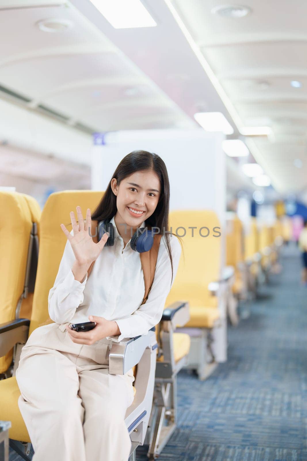 Young asian attractive woman travel by airplane, Passenger wearing headphone putting hand baggage in lockers above seats of plane by Manastrong