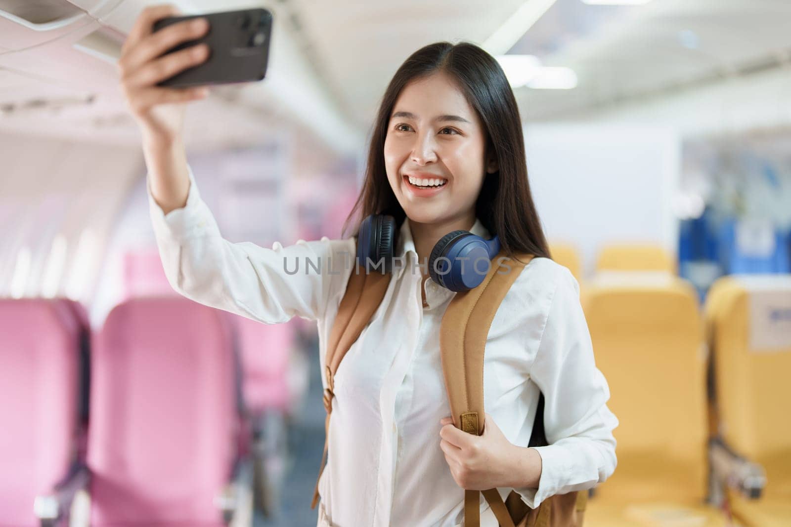 Asian business woman passenger sitting on business class luxury plane while working using smart phone mobile talking or video conference and travel concept.