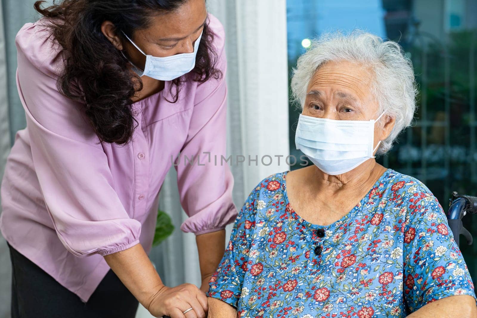 Caregiver help Asian senior woman on wheelchair and wearing a face mask for protect safety infection Covid19 Coronavirus. by pamai