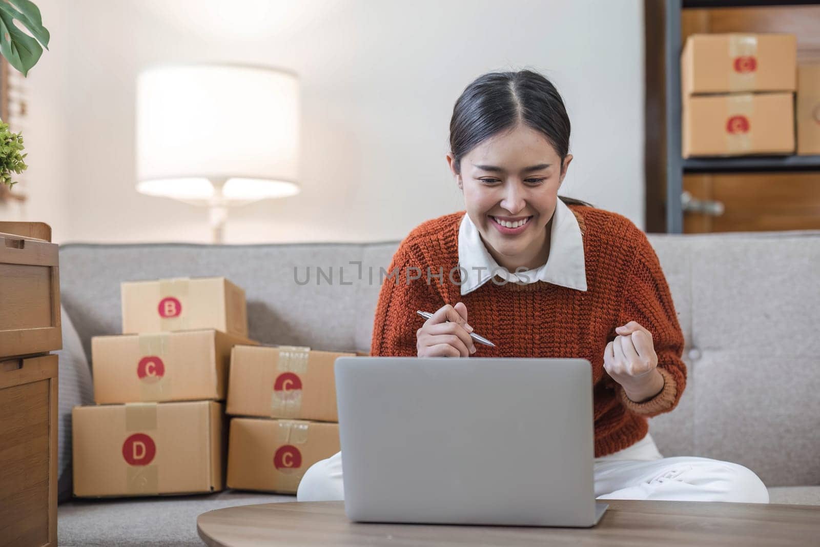 Asian business woman leaning on the sofa use laptop computer checking customer order online shipping boxes at home. Starting Small business entrepreneur SME. Online business, Work at home concept...