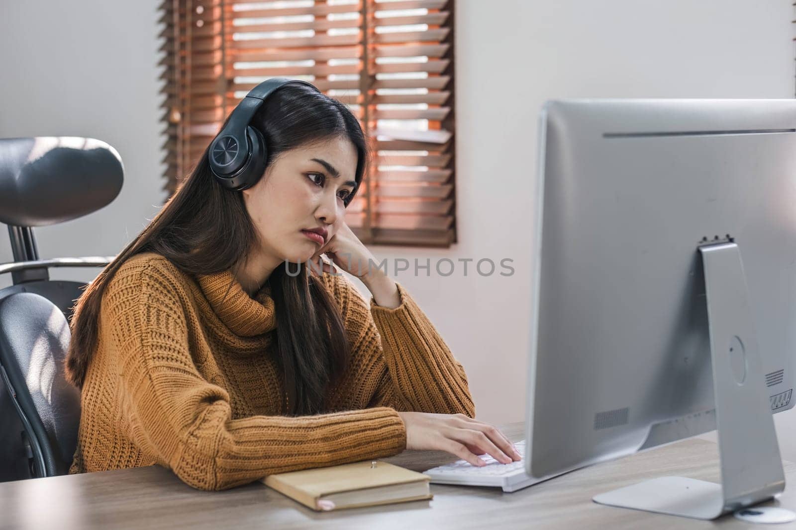 Tired teen asian lady in headphones falls asleep at table with laptop in room interior. Boring video lesson at home, problems at study, education with modern technology, online webinar and overwork..