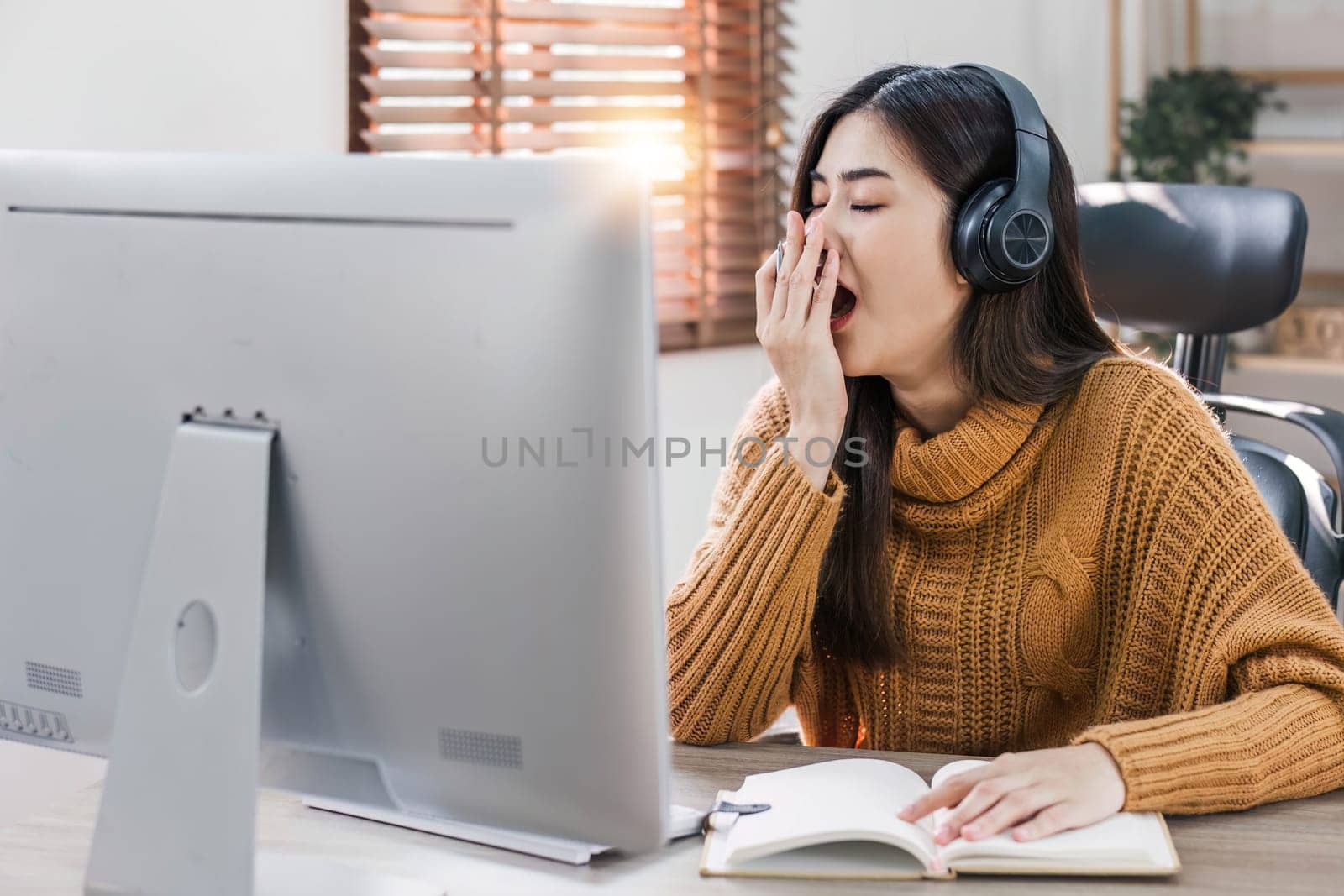 Tired teen asian lady in headphones falls asleep at table with laptop in room interior. Boring video lesson at home, problems at study, education with modern technology, online webinar and overwork..