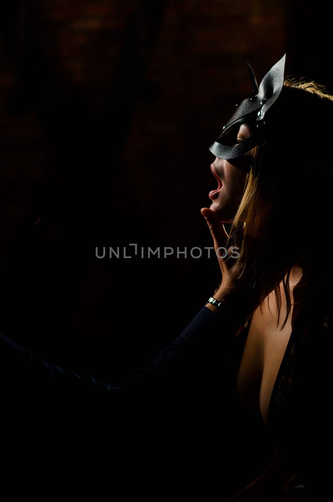 A man in a shirt holds his fingers on the sensual lips of a submissive lover. Portrait Woman in a leather cat mask. BDSM Games for adults.