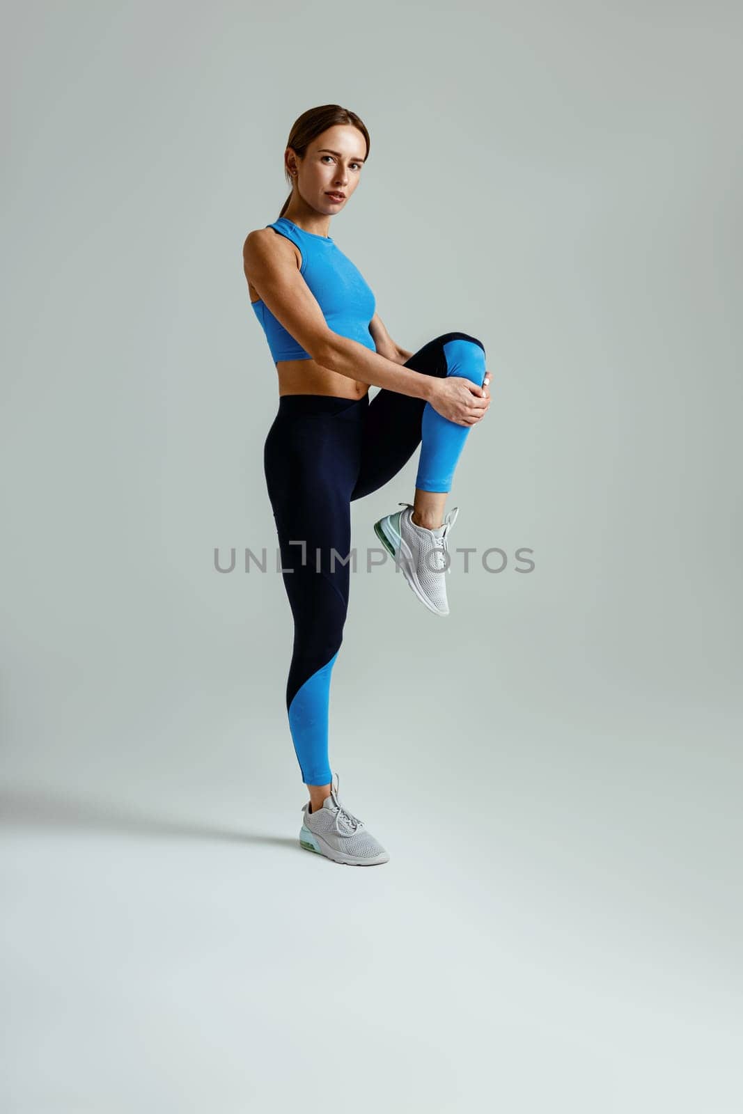Attractive sportswoman pull her leg, stretch for gym training on studio background