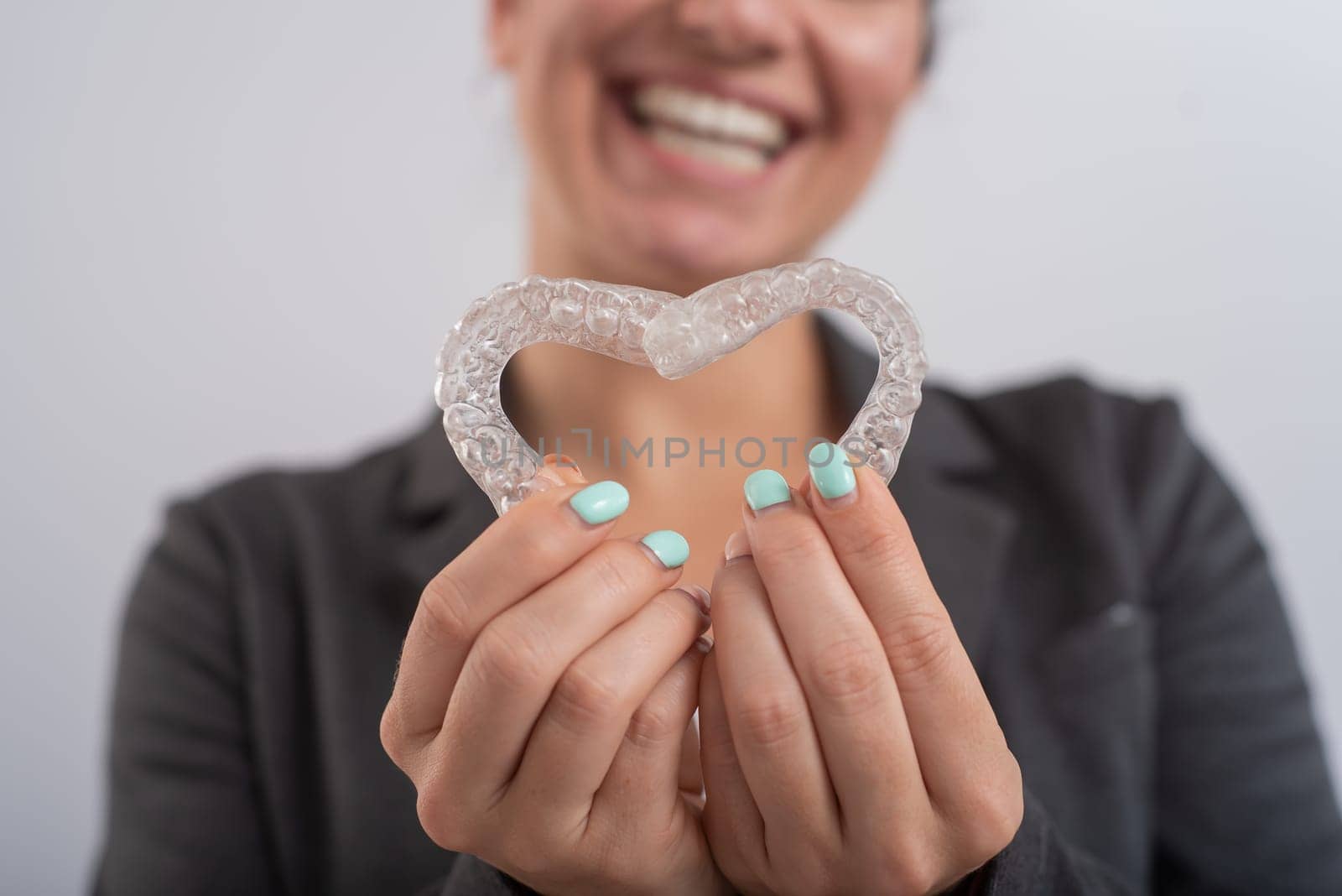 Caucasian woman holding two transparent heart-shaped aligners.