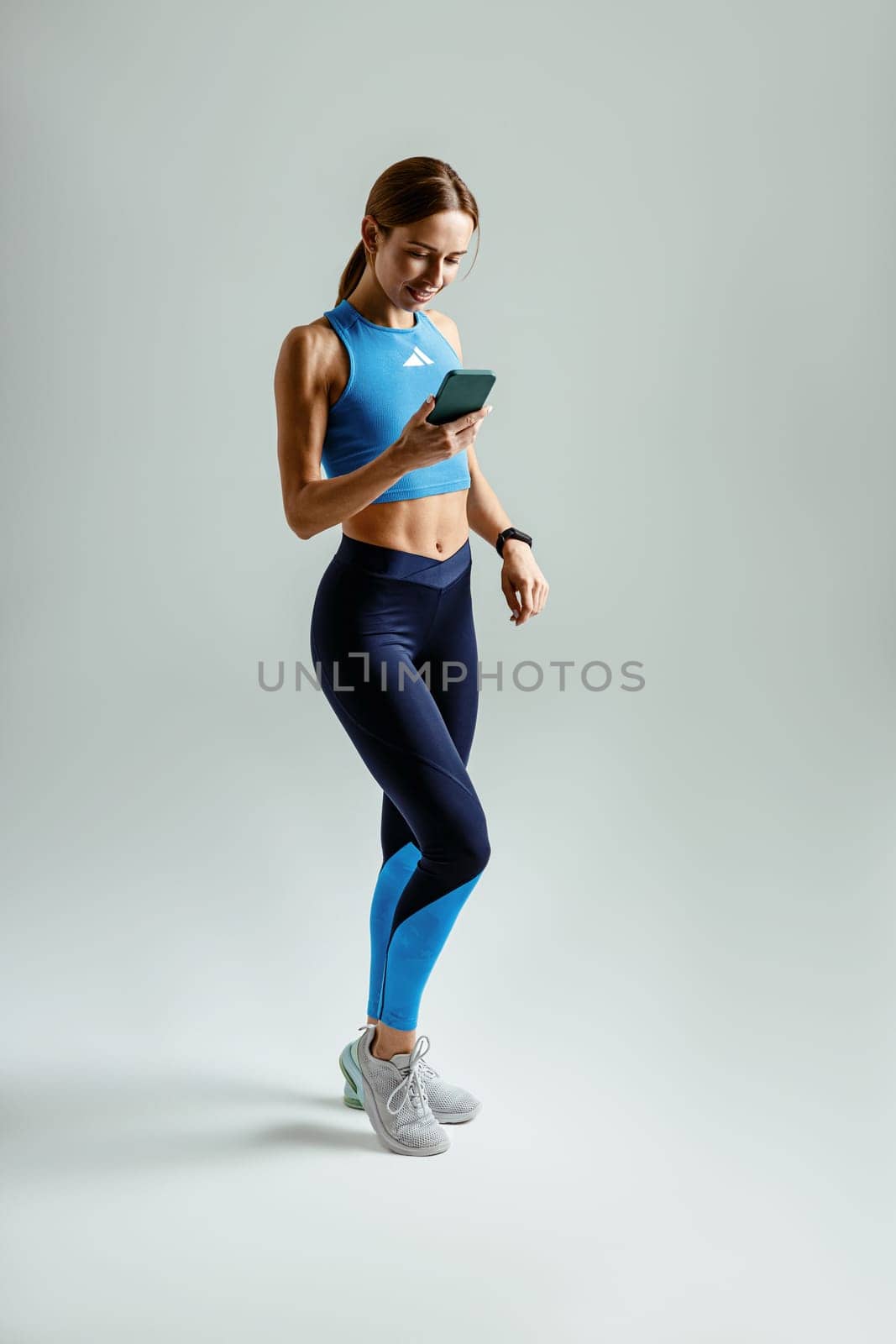 Athletic woman holding smartphone standing against studio background. High quality photo