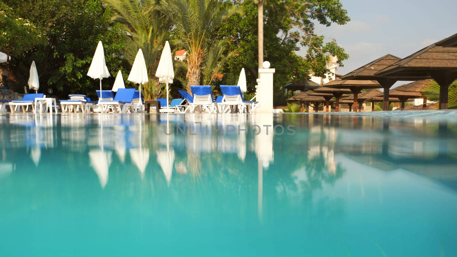 Empty sunbeds and closed parasols on morning, by the hotel pool. Photographed from water level. Vacation background, space for text down.