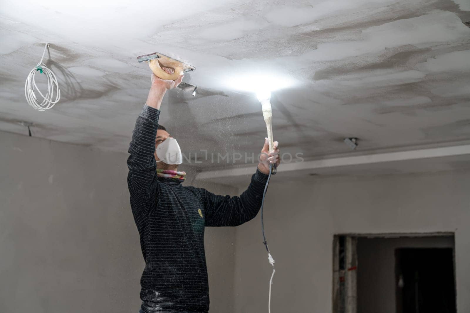 sanding a plasterboard ceiling in a new building with a trowel by Edophoto