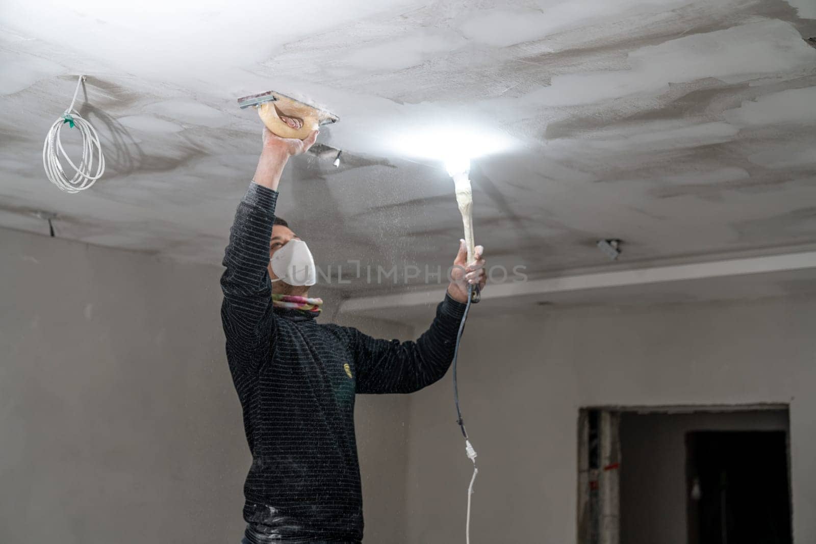 sanding a plasterboard ceiling in a new building with a trowel. High quality photo