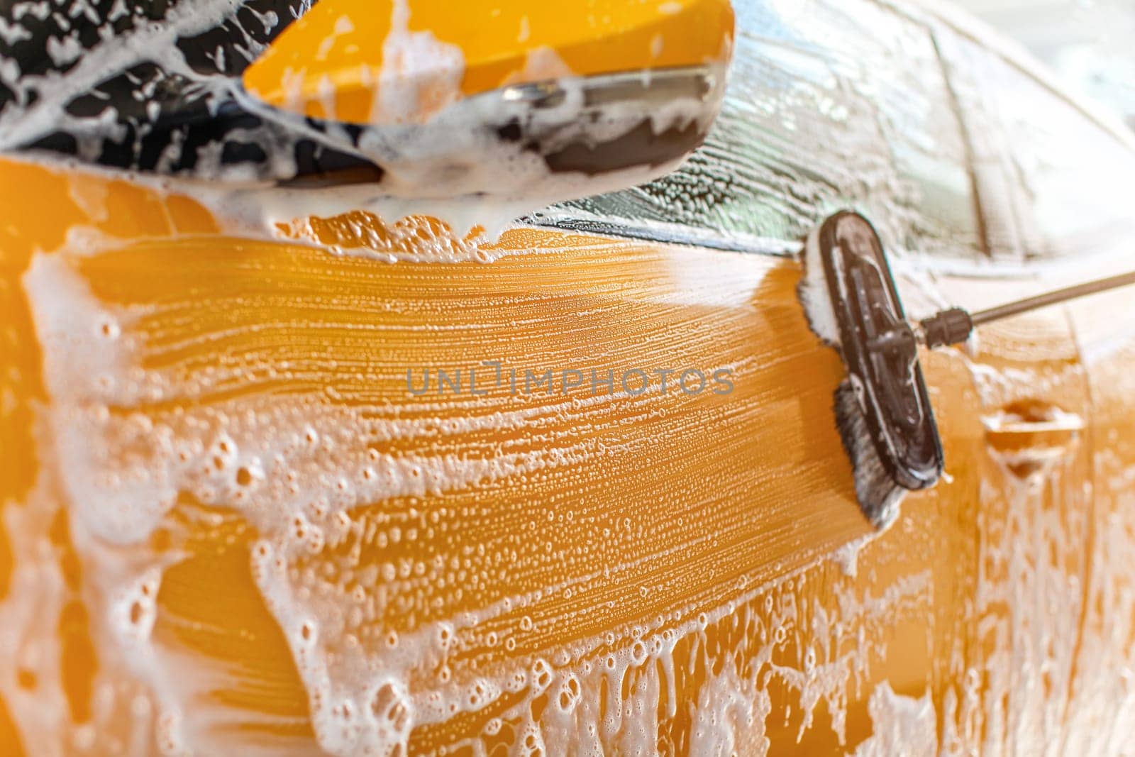 Side of car washed in self serve carwash, strokes from brush in white shampoo visible on yellow paint.