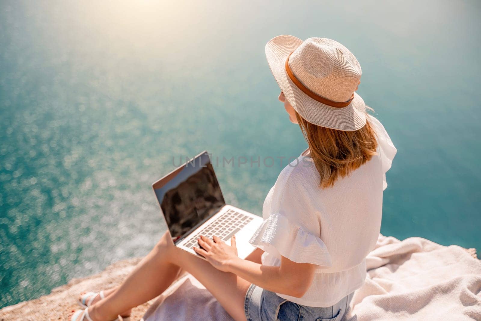 Freelance women sea working on the computer. Good looking middle aged woman typing on a laptop keyboard outdoors with a beautiful sea view. The concept of remote work