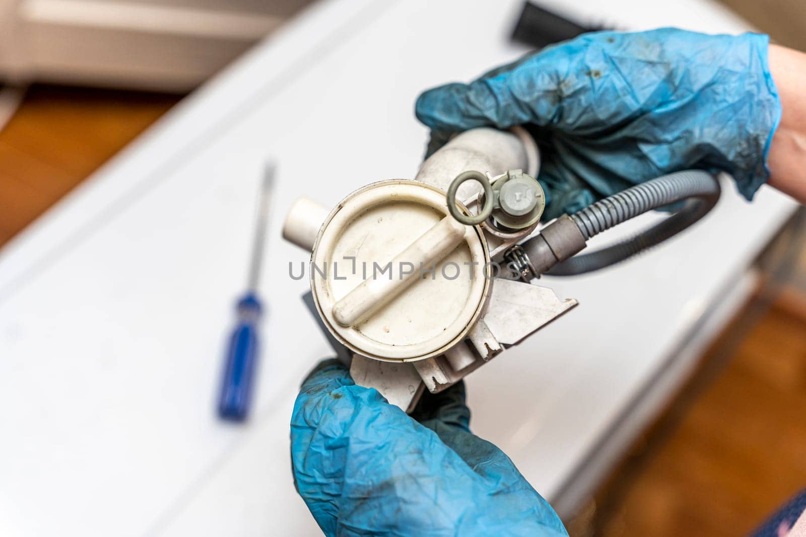 a broken old washing machine water pump in the hands of a home appliance repairman. Repair of a used washing machine. A jammed pump. calcium-magnesium deposits. Scum.