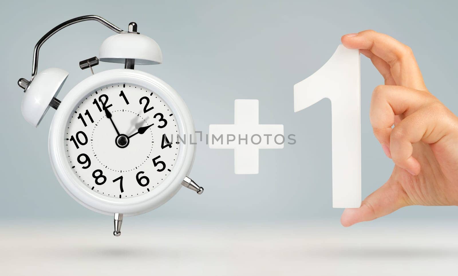 Change time. Spring forward, on a gray background. A white alarm clock indicates that the time has been moved forward an hour. Hand holding number one with plus sign, Spring forward concept.