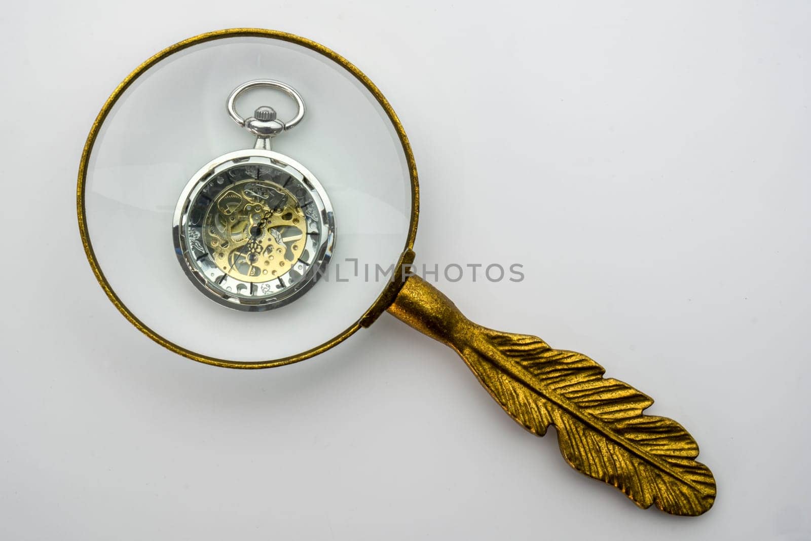 Gold handled magnifying glass viewing a silver modern pocket watch with visible gears, isolated on white background. High quality photo