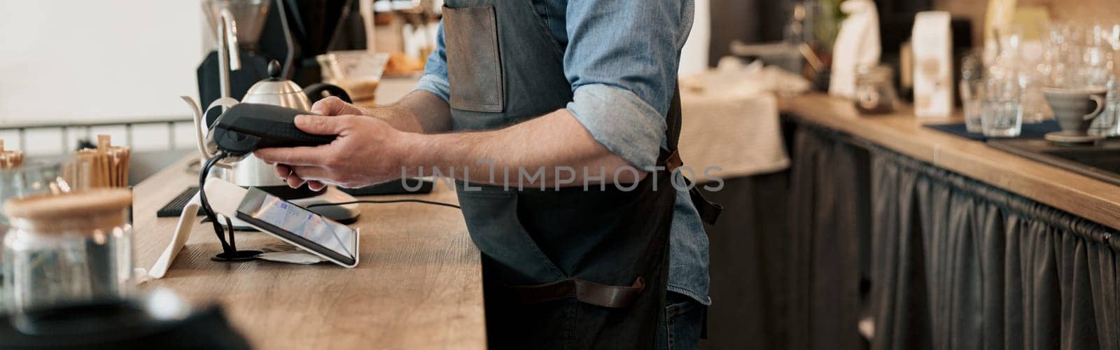 Smiling barista holding payment terminal while standing behind counter