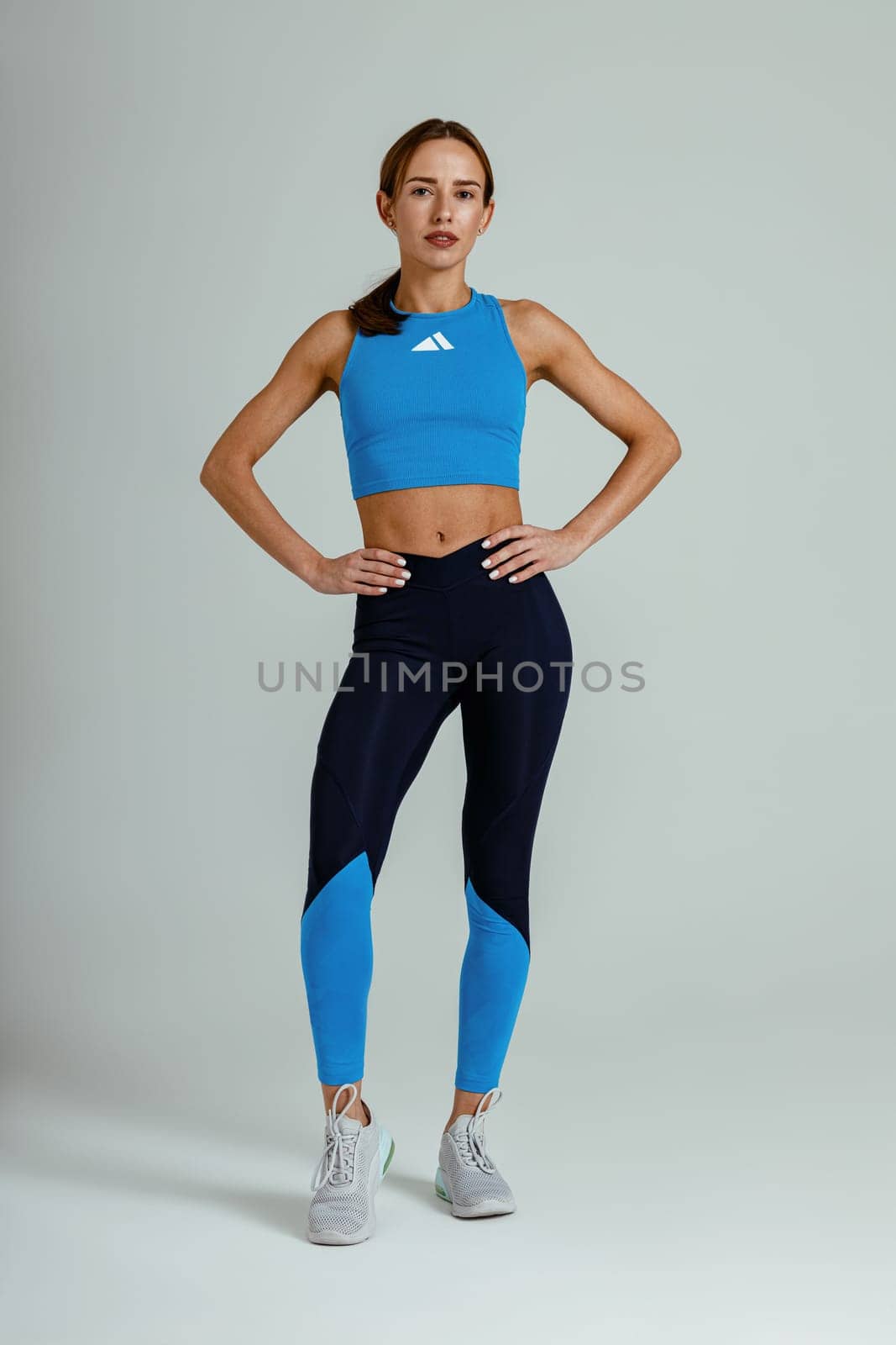 Strong attractive female fitness trainer in sportswear looking at camera on studio background by Yaroslav_astakhov