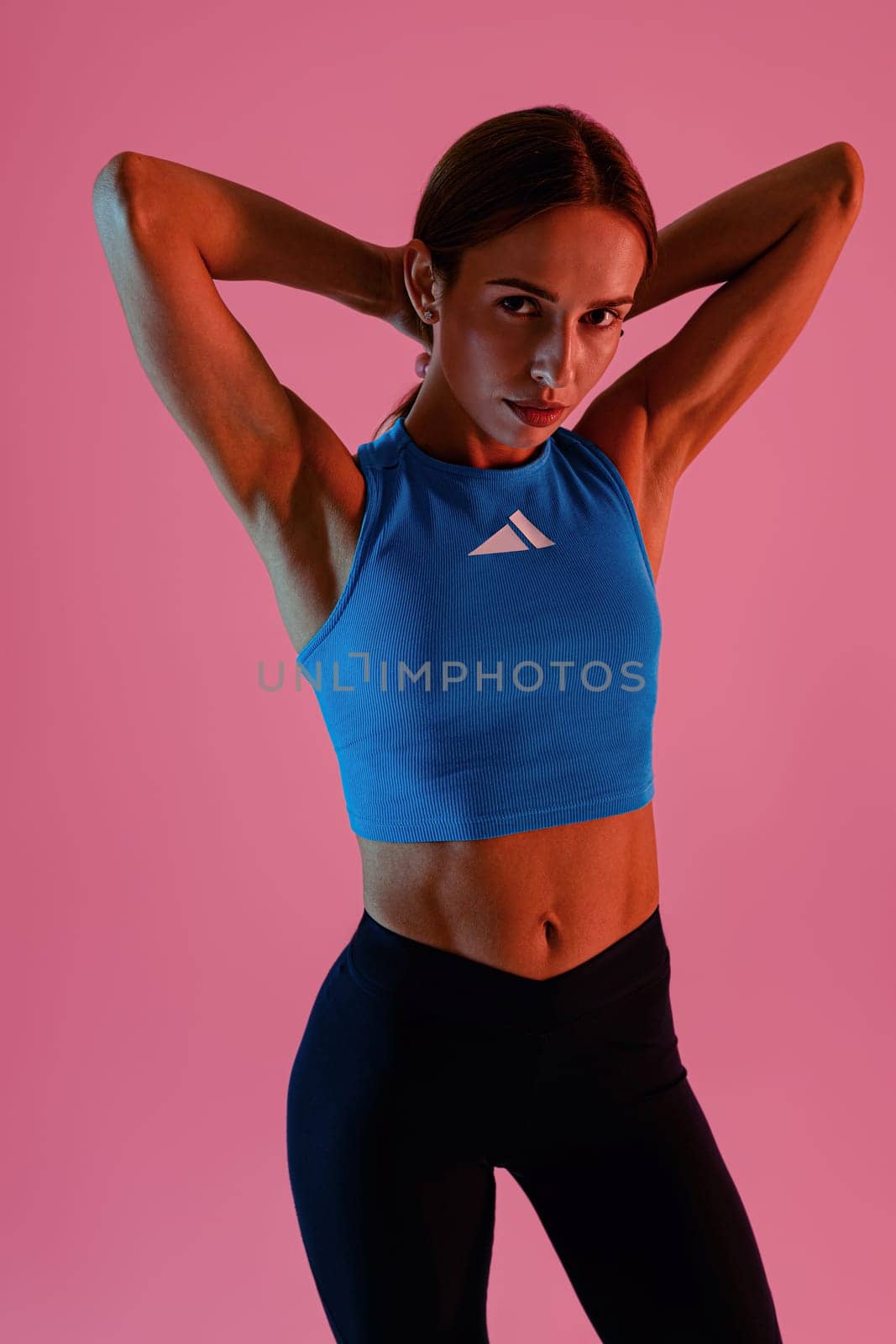 Beautiful fitness woman wearing sportswear posing over studio background and looking at camera by Yaroslav_astakhov