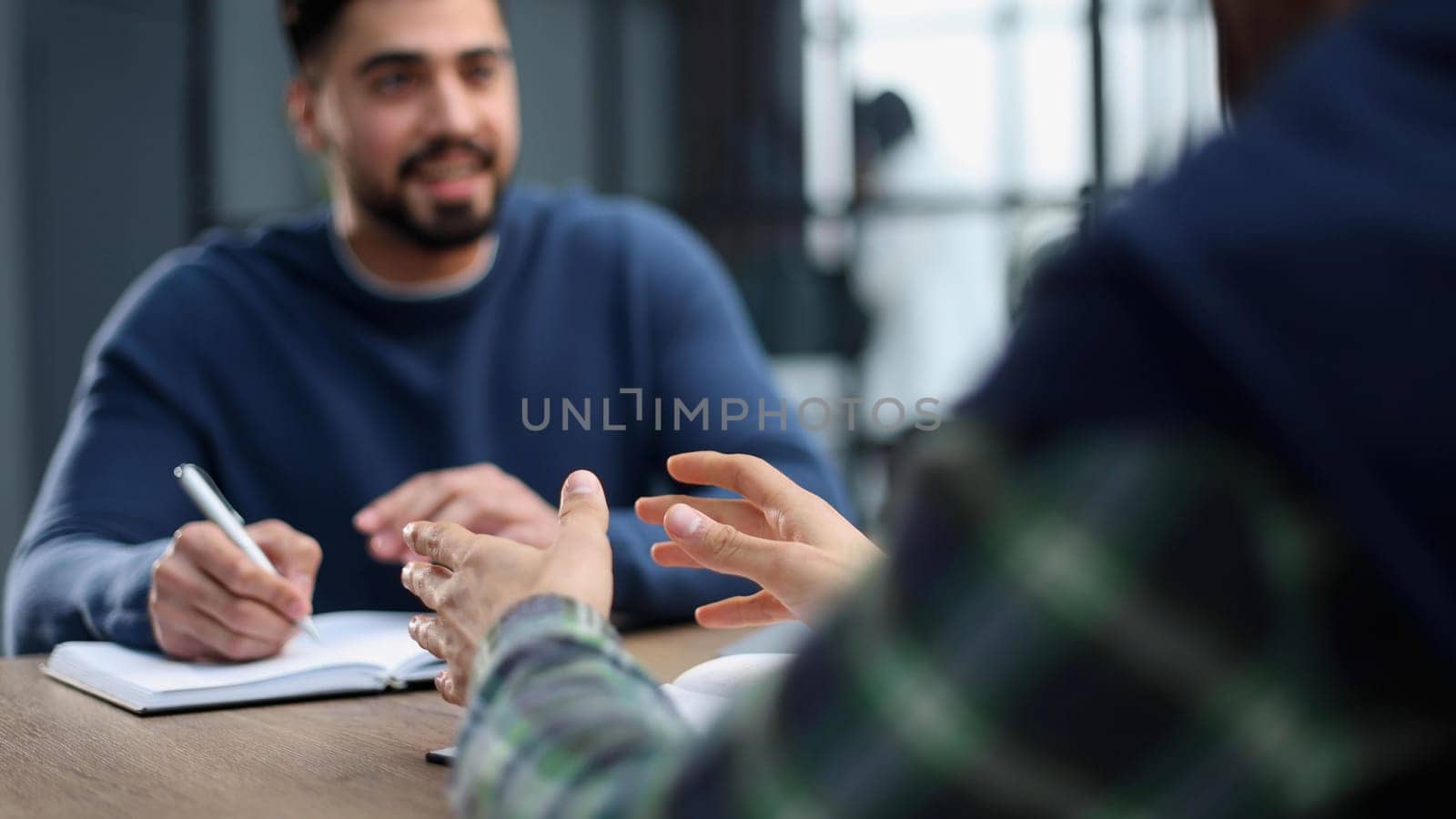 A young accountant working in the office communicates with a client and writes in a notebook.