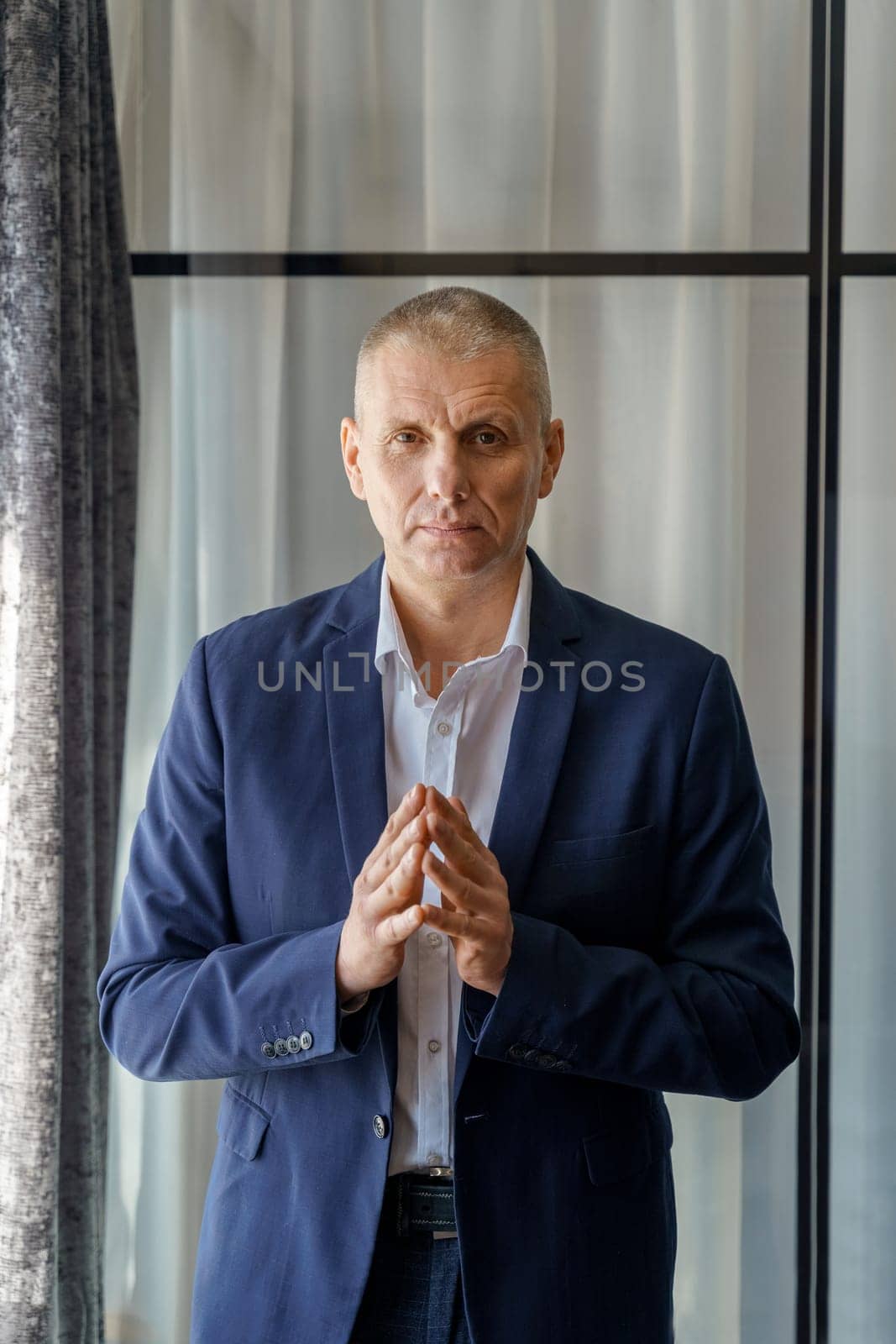 Portrait of a mature calm businessman with his jacket unbuttoned and palms folded in front.