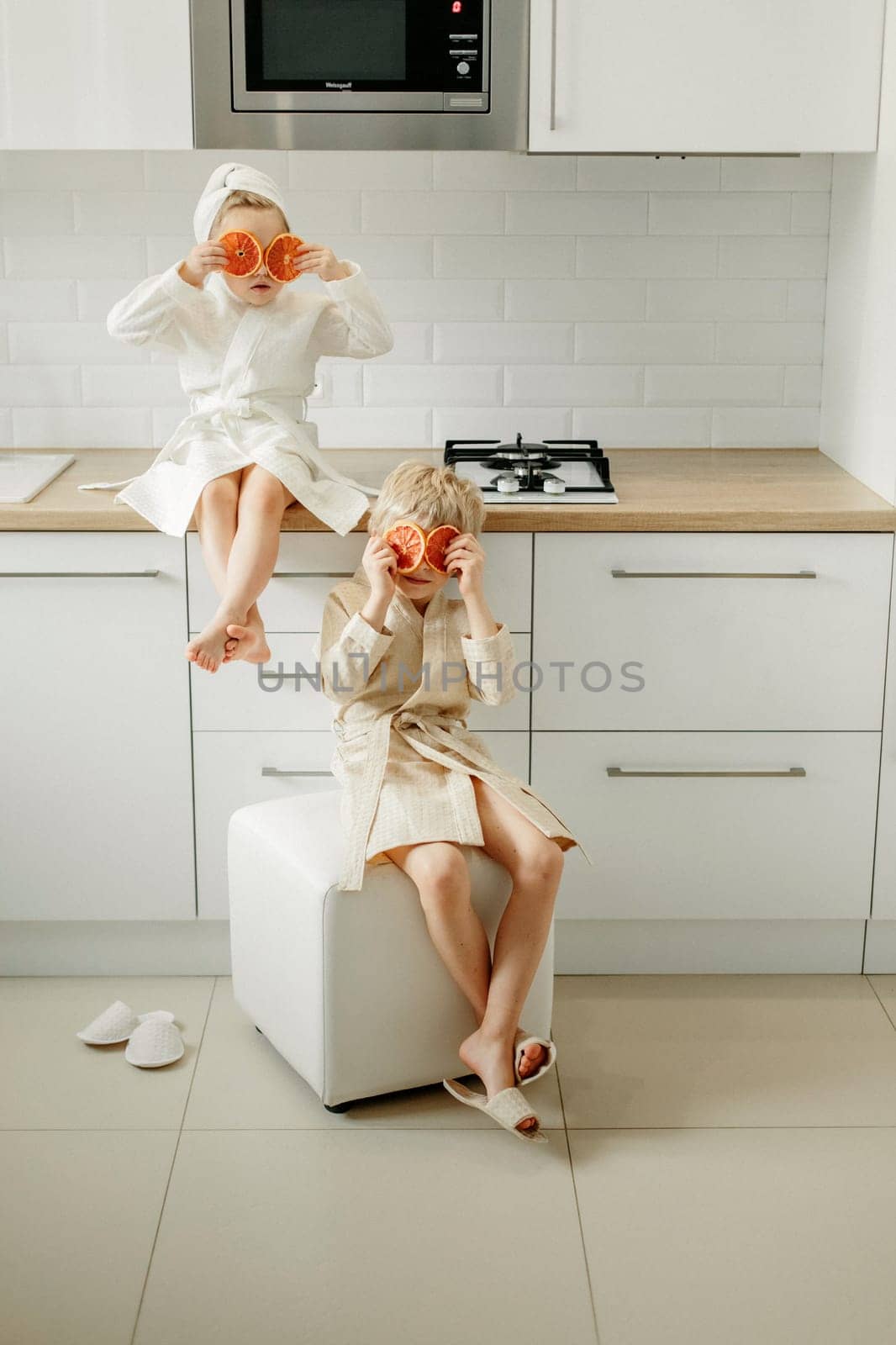 A girl and a boy in bathrobes sit in the kitchen and close their eyes with candied oranges.