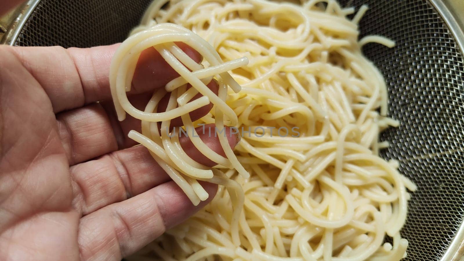 Yellow white thin strands of noodles in the metal bowl. Raw and uncooked. Cooking noodles in boiling water and rinsing vermicelli or spaghetti with water by woman hand