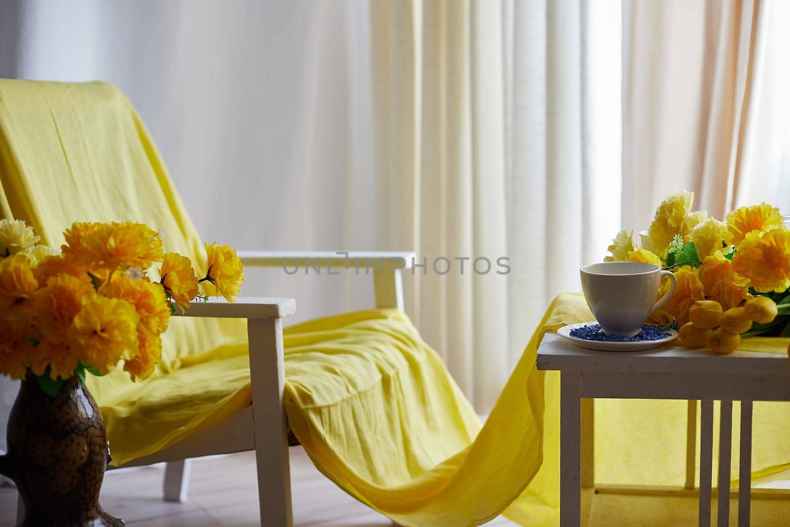 Interior in living room with armchair, table and flower by window with curtains in yellow colors. Empty location for shooting in photo studio. Concept of beauty, comfort and convenience, Partial focus