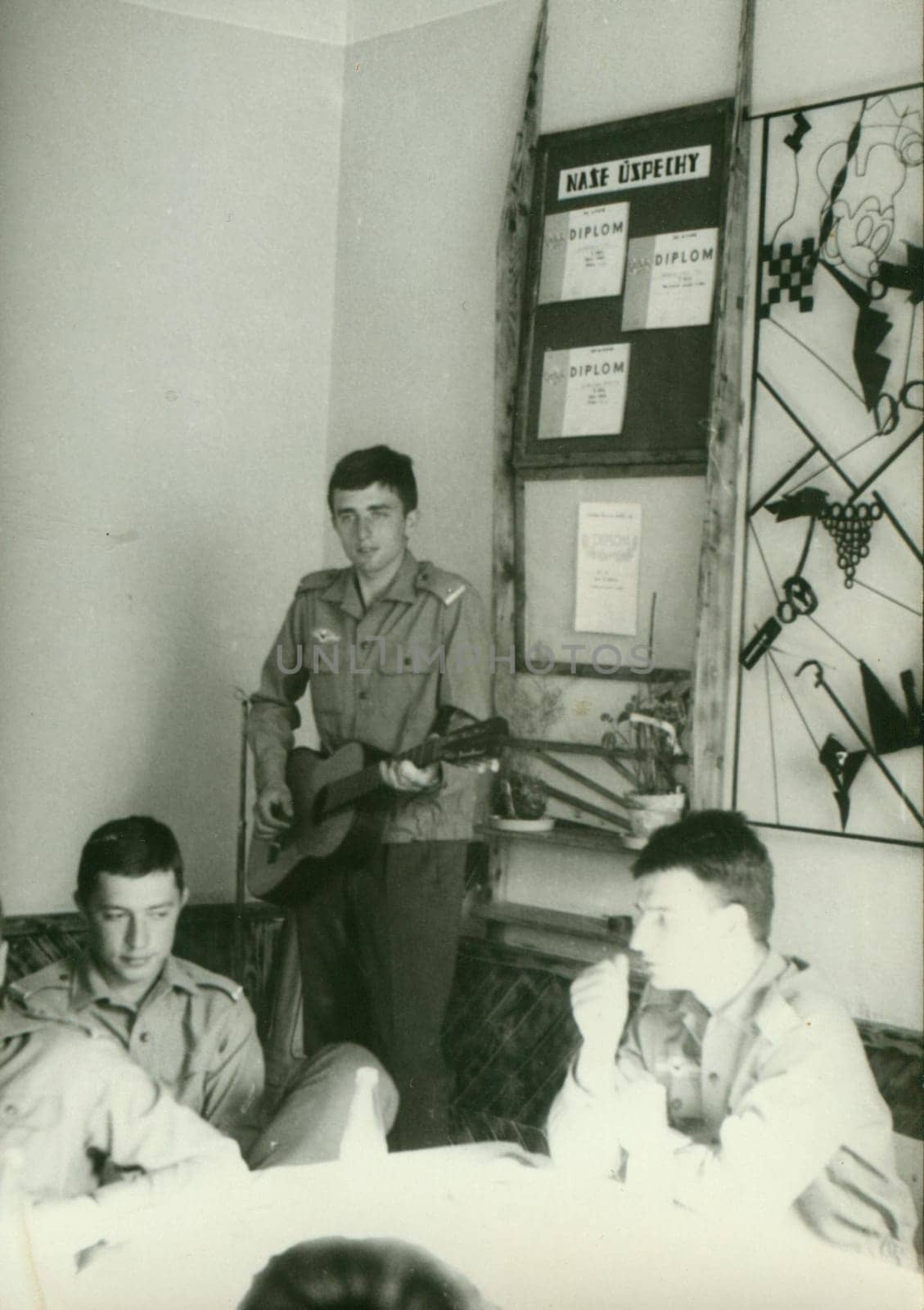 Retro photo shows young man - soldier plays the guitar. Vintage photography. Circa 1970. by roman_nerud